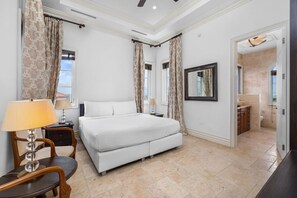 A hotel room with a bed, two bedside tables, a chair, a mirror, and a bathroom visible through an open door.