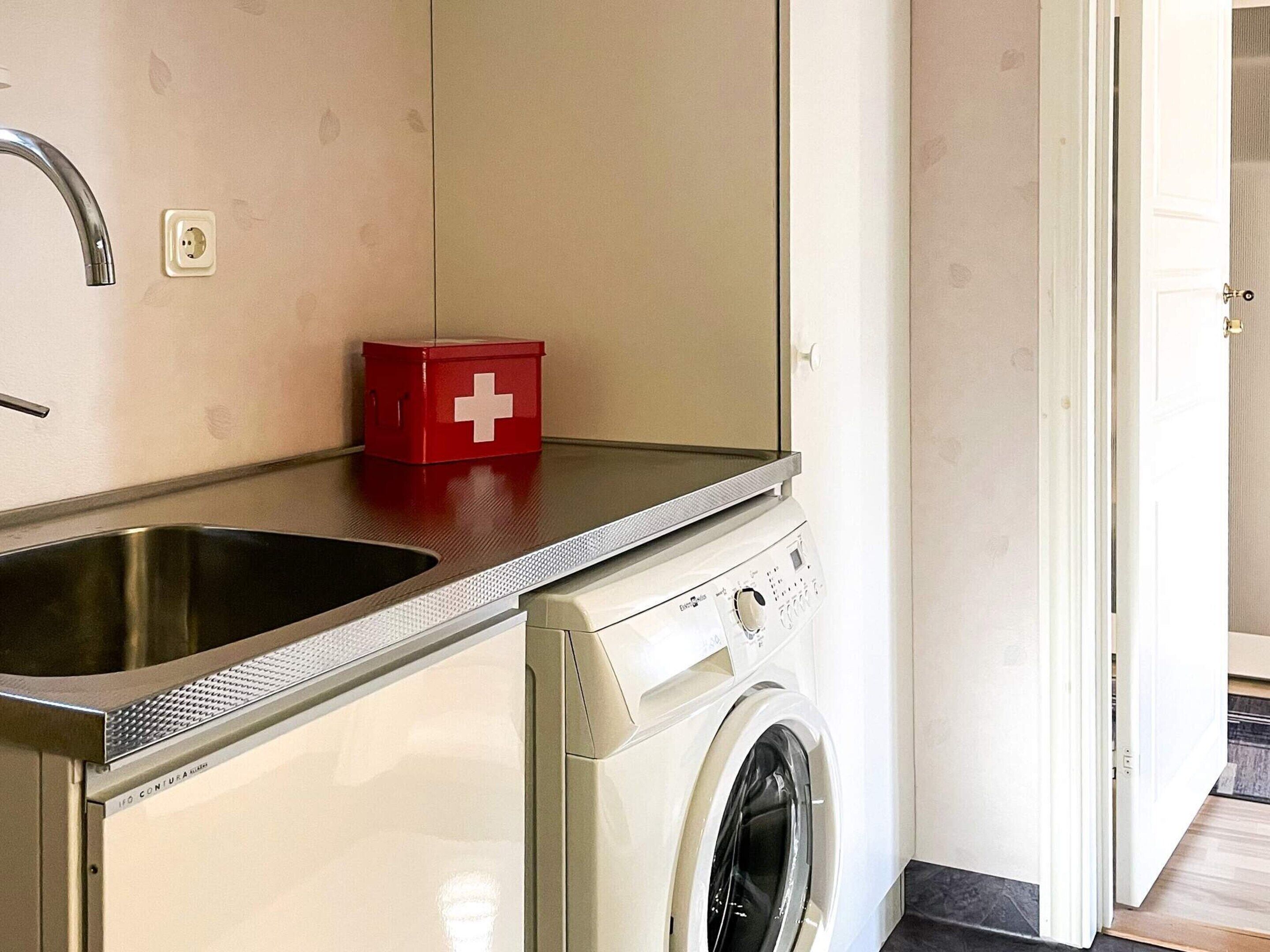 Cocina compacta con lavamanos, un botiquín de primeros auxilios rojo y lavadora.
