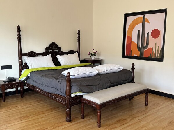 A four-poster bed with a grey and white bedding set, a bedside table with a phone, and a wall-mounted painting of a desert landscape.