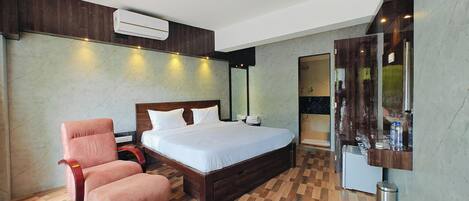 A bedroom with a bed, a chair, a vanity with a mirror, and an air conditioning unit.