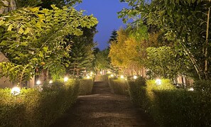 Un chemin pavé, bordé de haies et d’arbres soigneusement taillés, qui mène à un bâtiment.