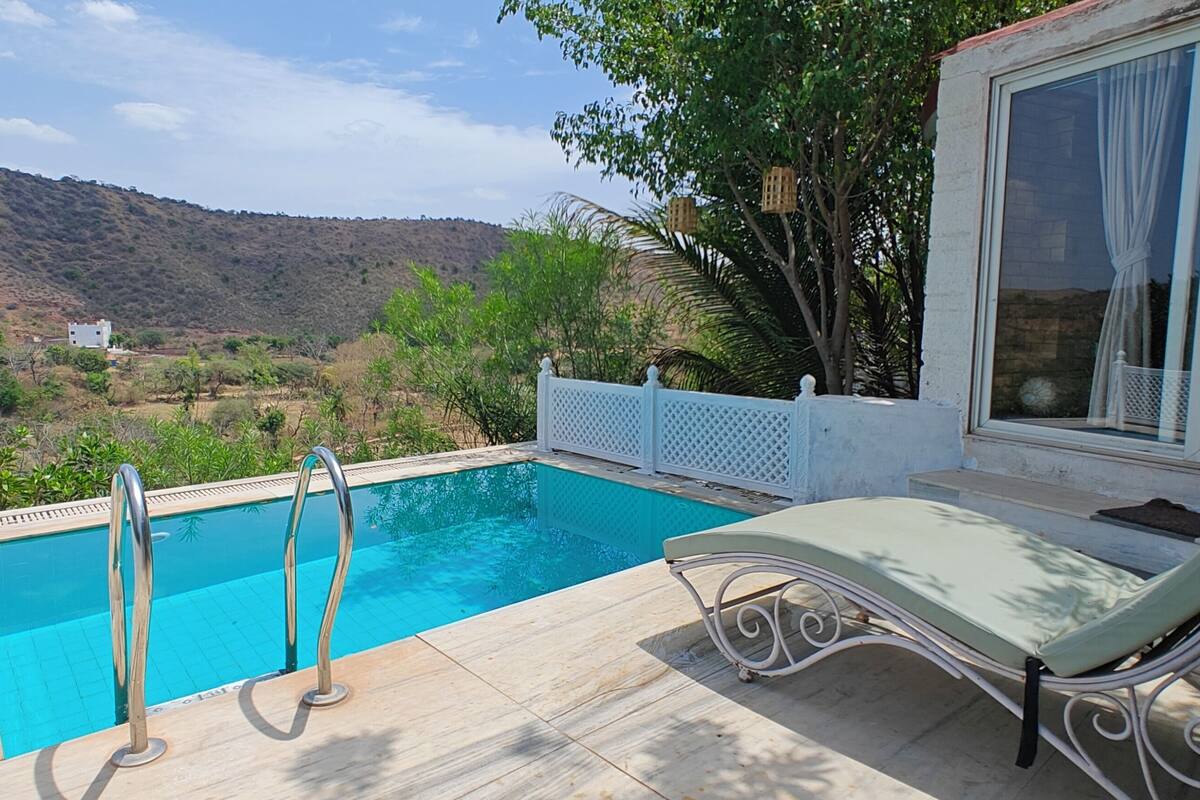 Une piscine avec vue sur un paysage vallonné, une clôture blanche et un fauteuil de relaxation.