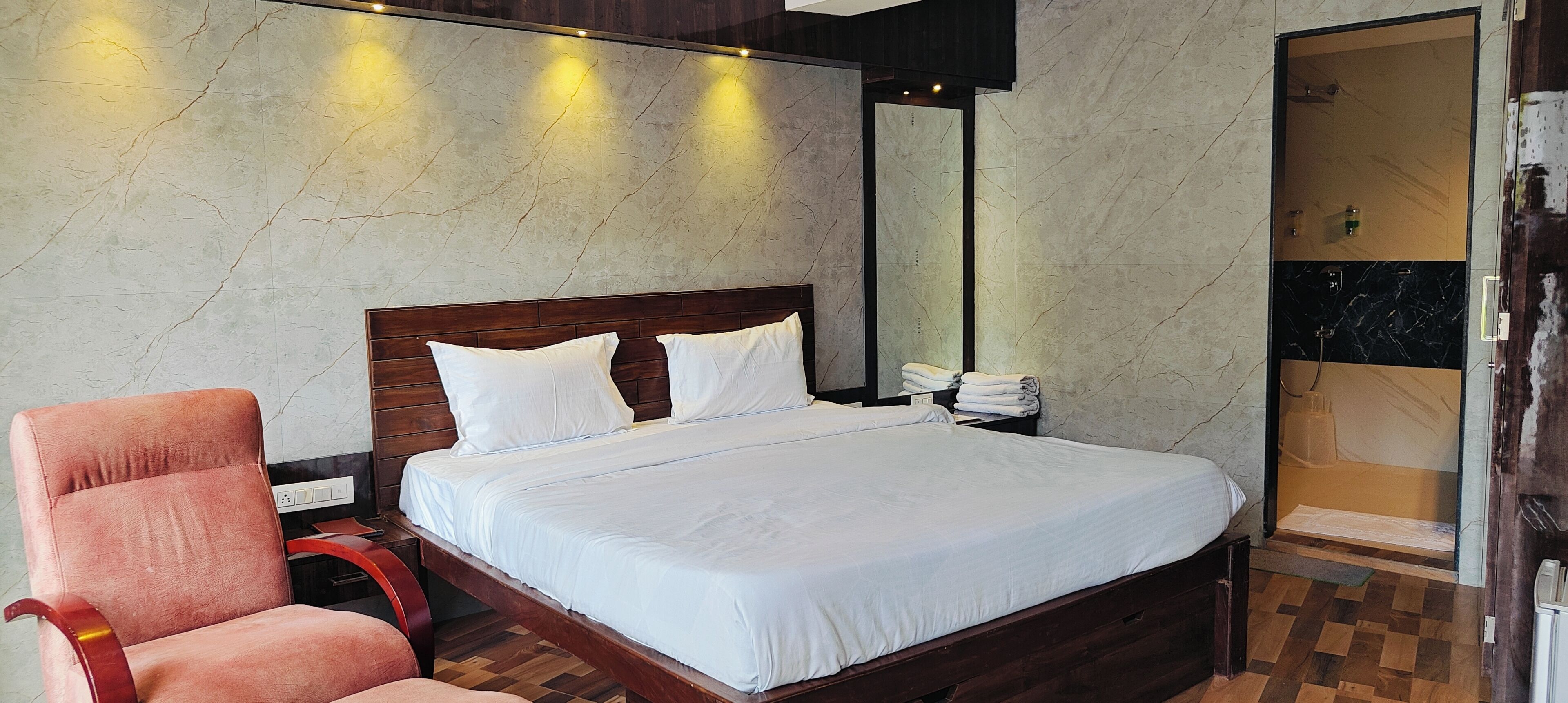 A hotel room with a wooden bed, a chair, a large mirror, and a shower area.