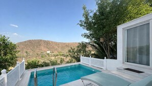 Une piscine avec vue sur un paysage vallonné, une clôture blanche et un espace détente doté d’une porte vitrée.