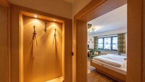 Een houten garderobe met een plank, een bed met wit beddengoed en een raam met gordijnen.