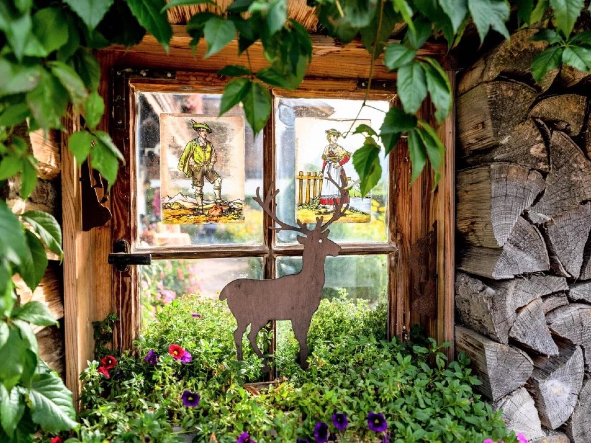 A rustic cabin with a wooden door, a deer decoration, and a window with two framed pictures.