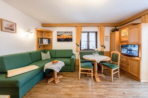 Una sala de estar acogedora con un sofá verde, una mesa de comedor con sillas, un televisor y armarios de madera.