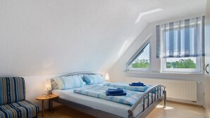 A bedroom with a bed, a nightstand, a chair, a window with curtains, and a view of greenery outside.