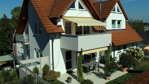 A two-story house with a sloped roof, a balcony, and a covered patio area.