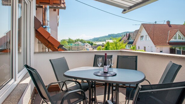 A balcony with a table and chairs, a bottle of wine, and glasses.