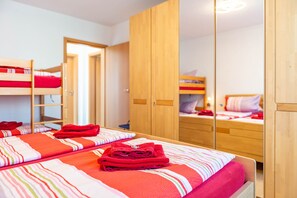 Una habitación con literas, un armario de madera y una cama con ropa de cama a rayas.