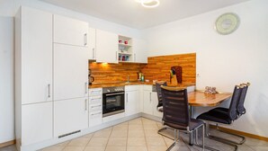 A modern kitchen with white cabinets, a wooden countertop, a built-in oven, and a dining area with a wooden table and black chairs.