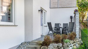 A patio with a table and chairs, a stone wall, and a window.