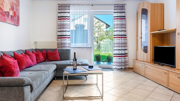 A living room with a sofa, a coffee table, a television, and a view of a garden through a window.