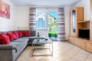Ein Wohnzimmer mit einer Couch, einem Couchtisch, einem Fernseher und Blick auf einen Garten durch ein Fenster.