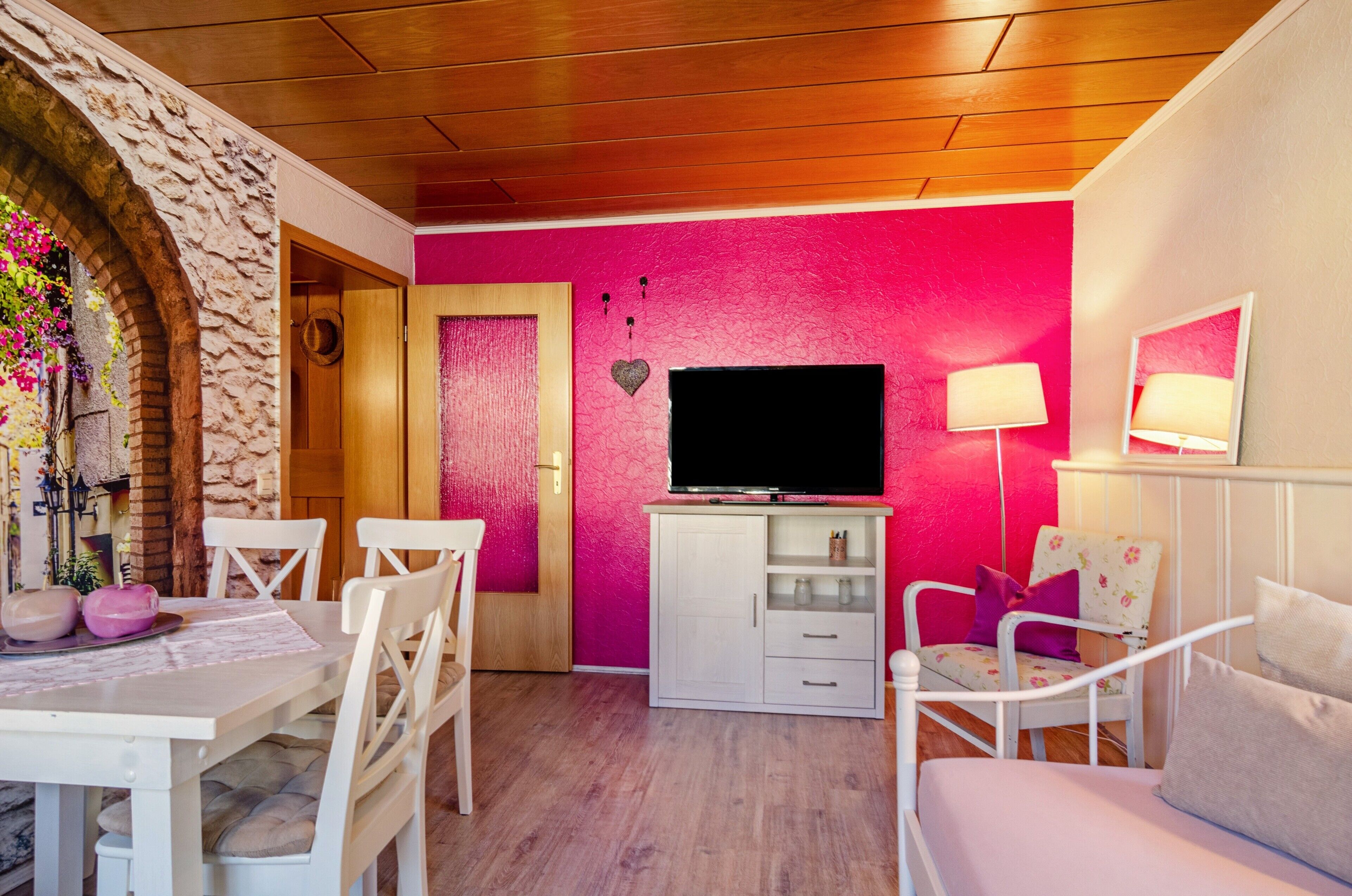 Ein Zimmer mit einem Steingewölbe, einem weißen Tisch mit Stühlen, einem Fernseher auf einem Schrank und einem Bett mit weißem Kopfteil.