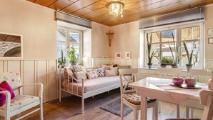 A cozy room with a bed, a dining table, chairs, a chandelier, and potted plants. - Fewo Alte Post, Apartment Rosenrot – Cozy Family Retreat in Meßstetten (Meßstetten)