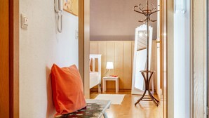 A hotel room with a wooden floor, a bench with a red pillow, a bedside table with a lamp, and a coat rack. - Fewo Alte Post, Apartment Rosenrot – Cozy Family Retreat in Meßstetten (Meßstetten)