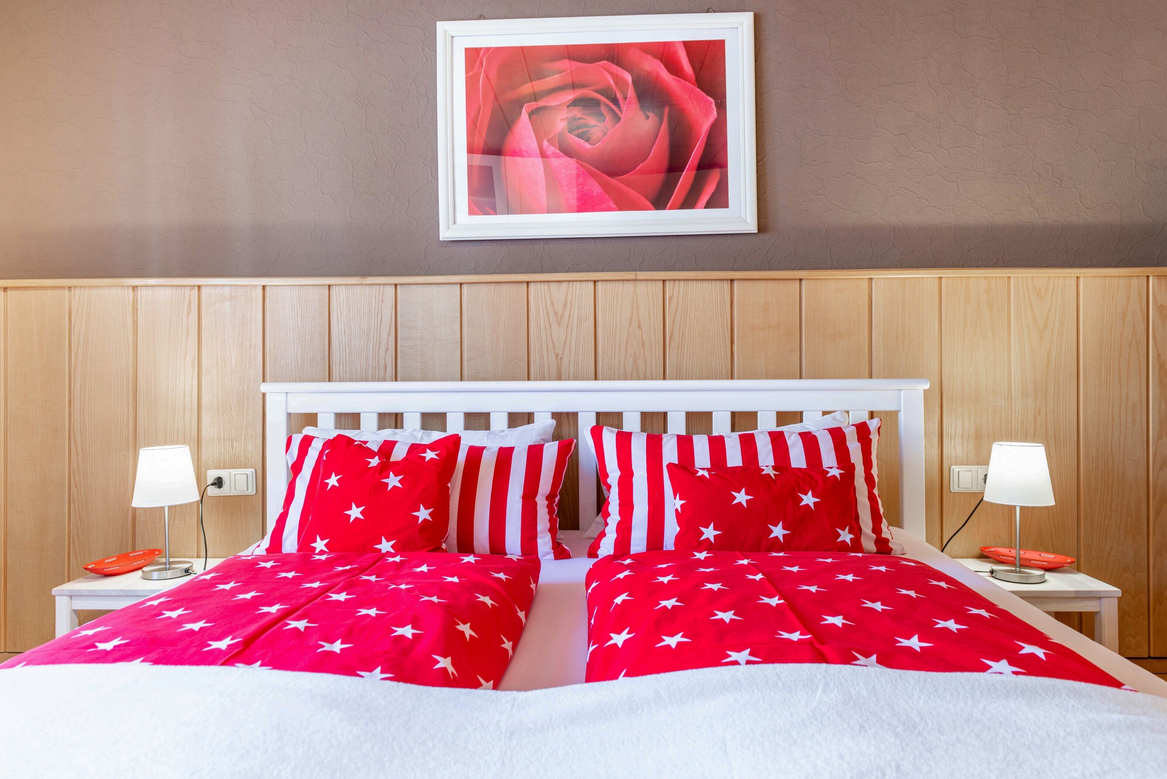 Ein Bett mit roter und weißer Bettwäsche, ein Holzkopfstück und ein gerahmtes Bild an der Wand.