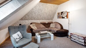 Ein Loft-Wohnzimmer mit Steinwand, einem braunen Ledersofa, einem Glastisch und einem grauen Sessel mit Kissen in Ankerform.