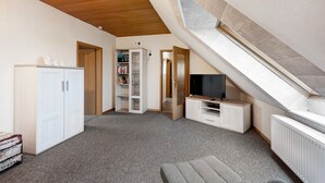 Ein Zimmer mit schrägem Dach, einem Fernseher, einem Bücherregal und einem Schrank.