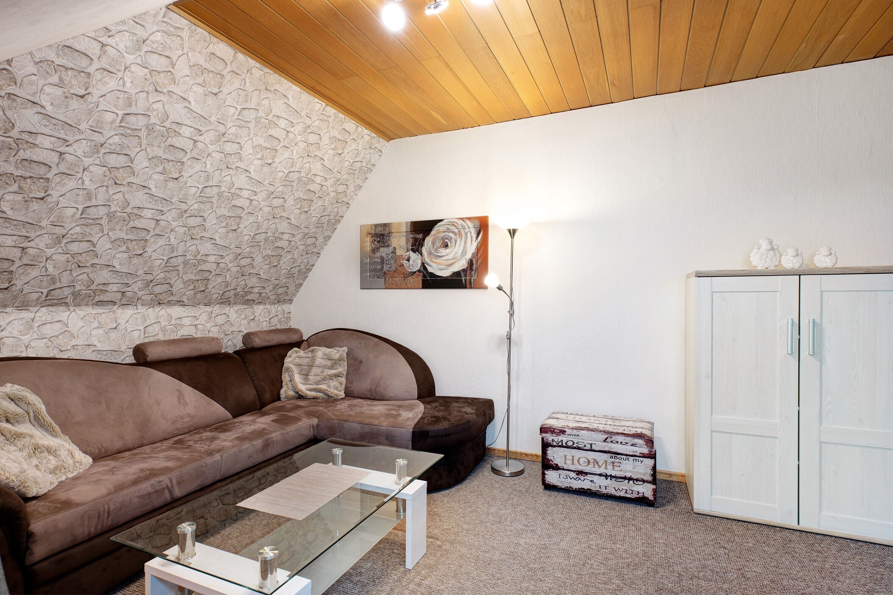 Een woonkamer met een stenen muur, een bruine bank, een glazen salontafel, een vloerlamp en een witte inloopkast.