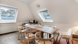 Ein Essbereich mit einem langen Tisch, sechs Stühlen und zwei Fenstern, die für natürliches Licht sorgen.