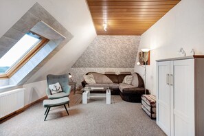 Un ambiente tipo loft con techo inclinado, ventana integrada, sofá, mesa de centro y un armario.