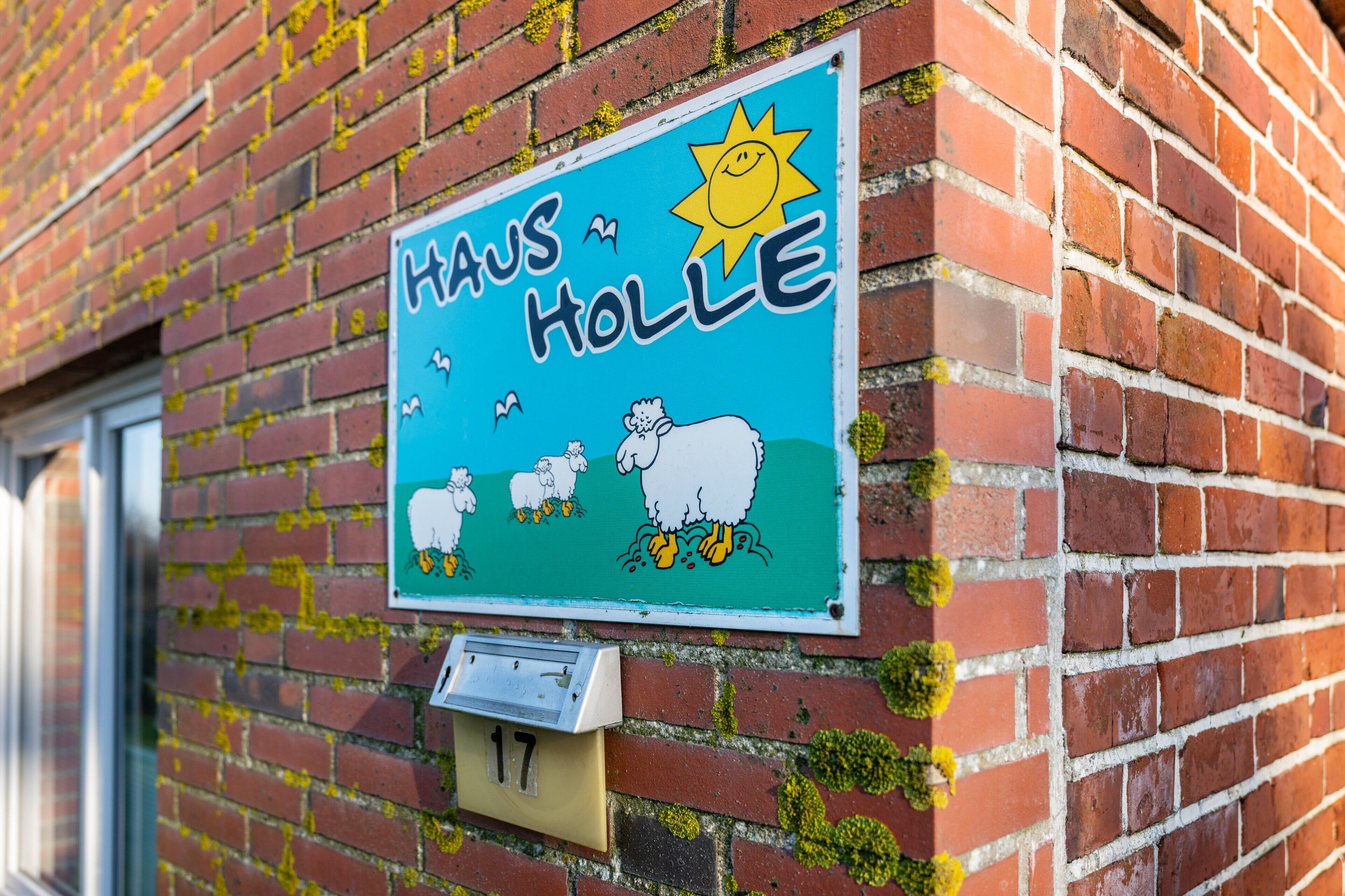 A house sign with a sun and sheep, a mailbox, and a brick wall.