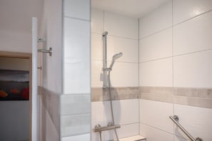 Ein Badezimmer mit weißen Fliesen, einer Dusche inklusive Duschbrause und einer Haltestange.