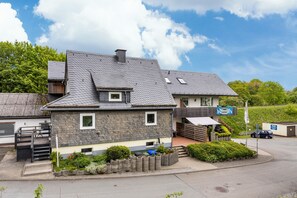 A two-story house with a sloped roof, a small porch, and a front yard with plants.