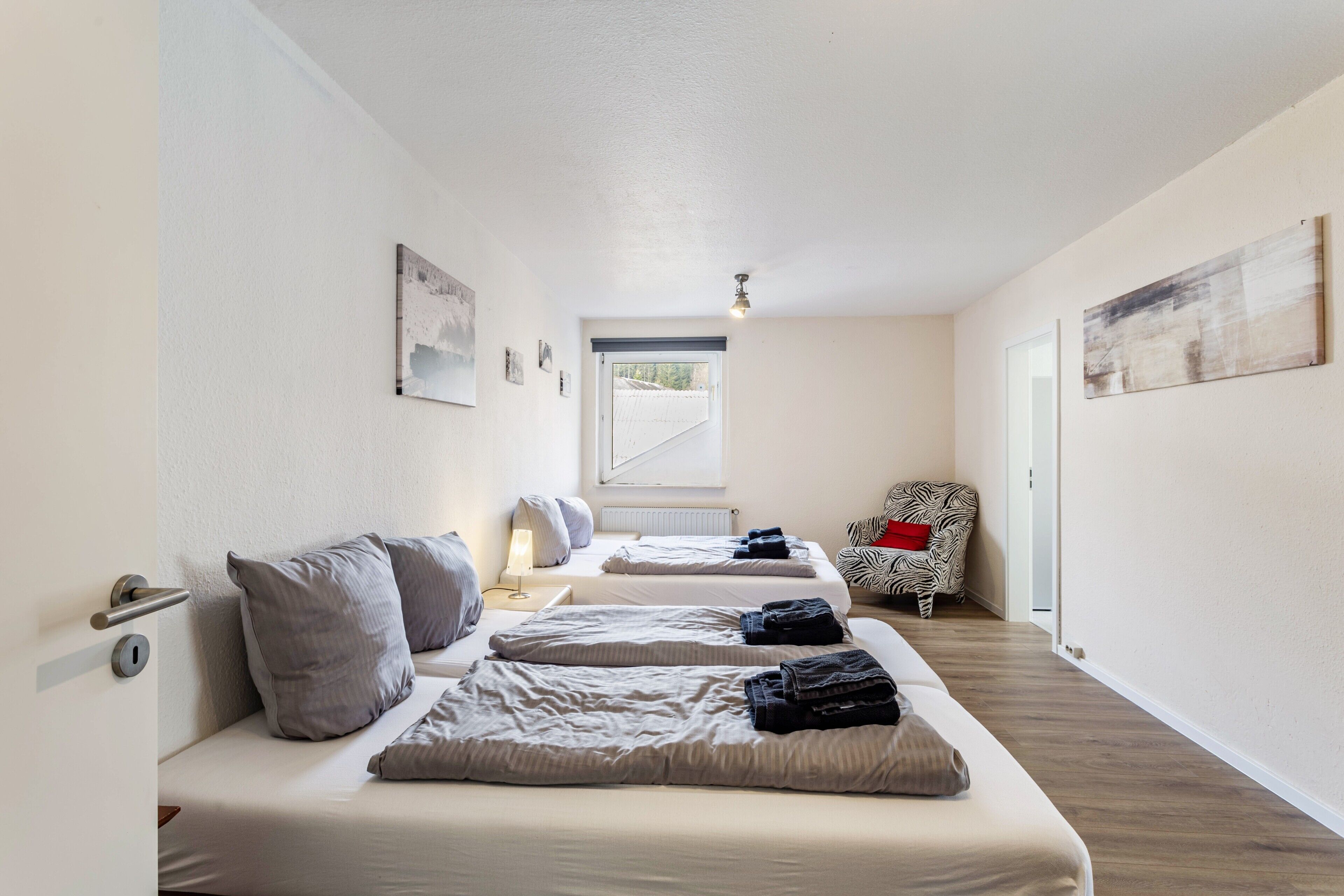 Une pièce avec deux lits, une chaise à motifs zébrés, une porte et une fenêtre.