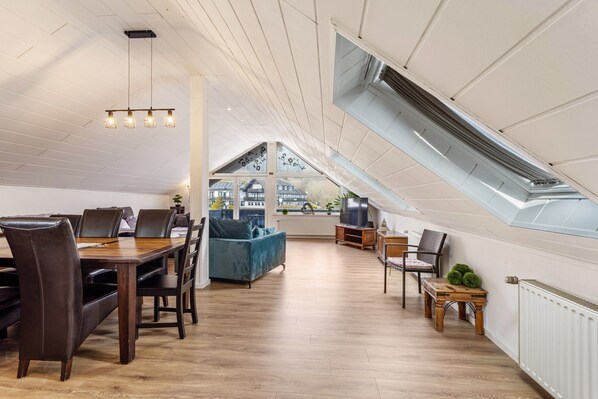 A spacious loft with a dining area, a sofa, a TV, and a skylight.