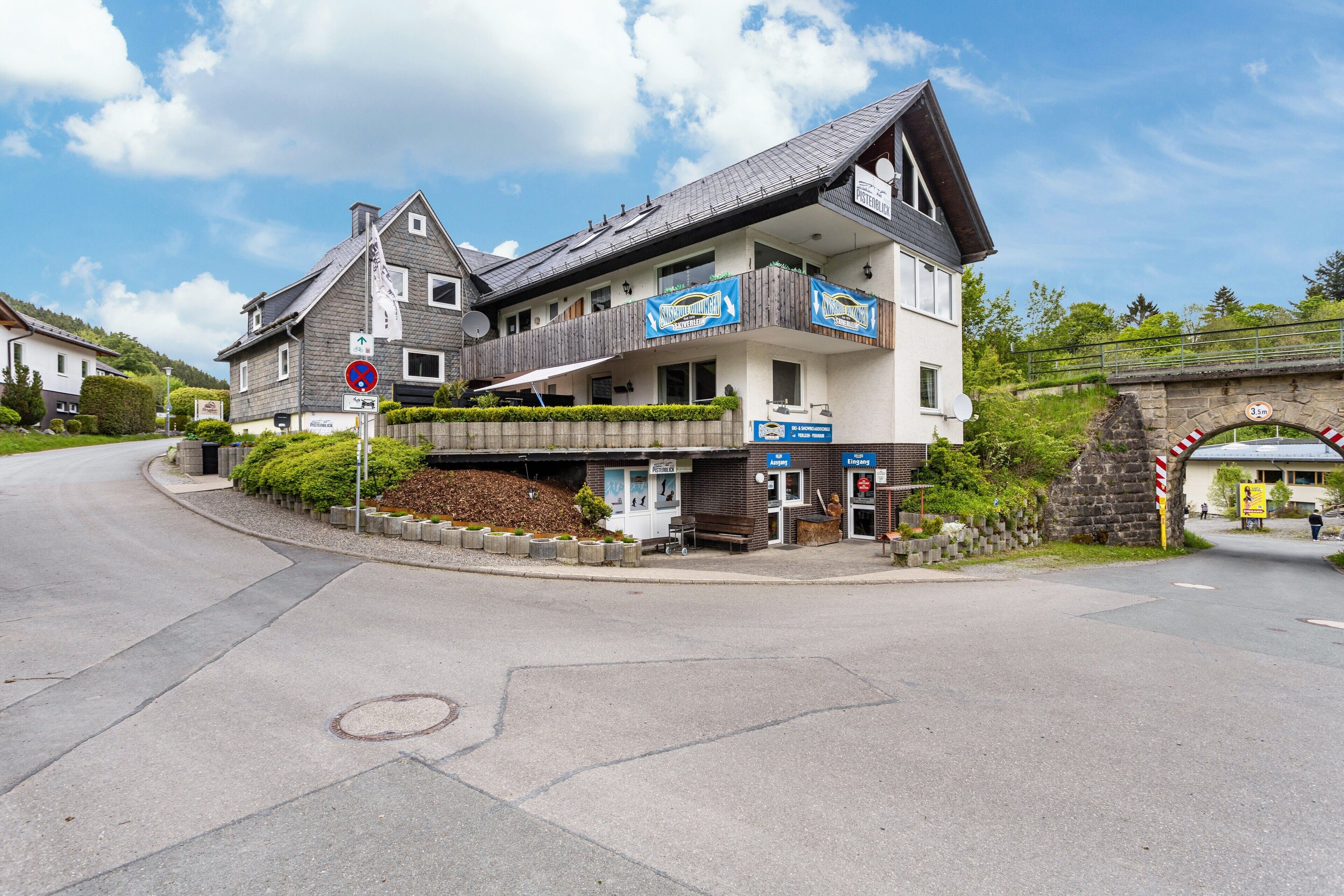 A multi-story hotel with a balcony, a signboard, and a stone bridge in the background.