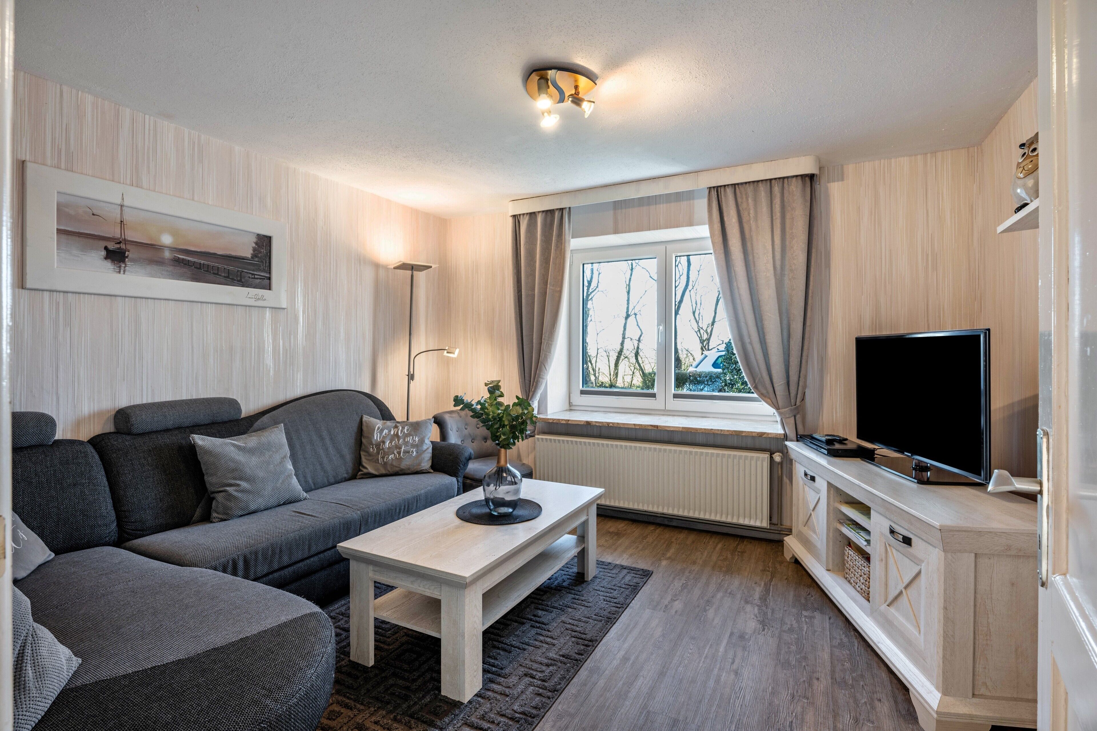 En moderne stue med sofa, sofabord, fjernsyn og et vindue med gardiner.