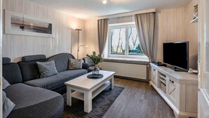 Un salón moderno con sofá, mesa de centro, televisor y ventana con cortinas.