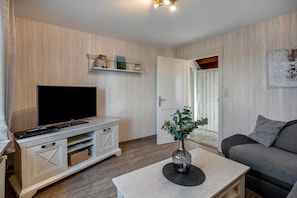 A living room with a TV, a sofa, a coffee table with a vase, and a wooden cabinet.