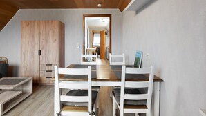 Un coin repas avec une table en bois et des chaises blanches, une armoire en bois, et une vue sur une autre pièce.