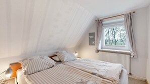 Une chambre à coucher avec un lit, une table de chevet, une lampe, une fenêtre avec des rideaux et un radiateur.