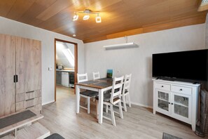 Un comedor con una mesa de madera, sillas blancas, un televisor y un aparador con puertas de cristal.