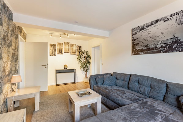 A modern living room with a grey sofa, a small coffee table, a lamp, and a painting on the wall.