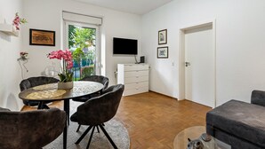 A dining area with a round table, chairs, a potted plant, and a flat-screen TV mounted on the wall.