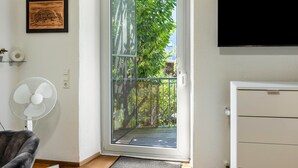 A room with a sliding glass door leading to a balcony, a white fan, a framed picture, and a mounted TV.