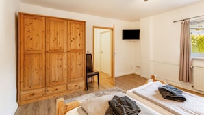 A bedroom with a wooden wardrobe, a single bed, a chair, a television, and a window with curtains. - Apartment 'Piste 4' with Shared Terrace, Balcony and Wi-Fi (Willingen (Upland))