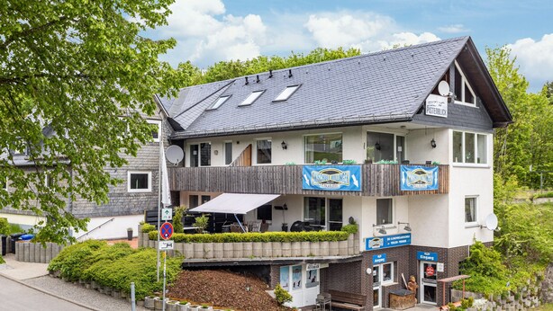 A two-story building with a balcony, signage for a restaurant, and a small outdoor seating area. - Apartment 'Piste 4' with Shared Terrace, Balcony and Wi-Fi (Willingen (Upland))
