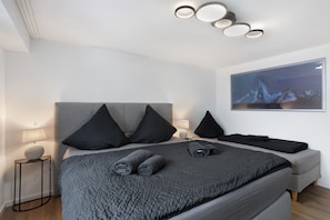 Une chambre moderne avec un grand lit, des lampes de chevet, une œuvre d’art accrochée au mur et une table ronde avec une lampe.