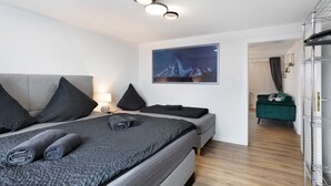 Et moderne soveværelse med en seng, sengeborde, et maleri og en grøn sofa i baggrunden.