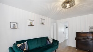 En moderne stue med en grøn sofa, et træskab og tre vægmonterede hylder med planter.