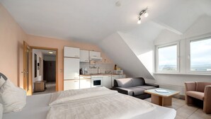 Habitació d'hotel moderna amb un llit gran, una cuineta, zona de seients amb taula i vistes per grans finestres.