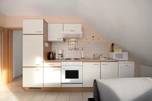 Une cuisine compacte avec des meubles blancs, un four encastré, un four à micro-ondes et une machine à café.